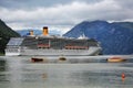 A large white cruise line or ship with Tourists in a rocky bay sail past small multi-colored fishing boats Royalty Free Stock Photo