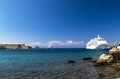 A large white cruise liner stands on a dock in a picturesque tourist port on the Greek island of Rhodes