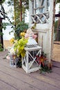 Large white decorative candle lantern and small candle lantern stand on terrace with flowers and autumn leaves. Wedding decor.