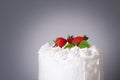 Large white delicious cake with cream and decorated with strawberries and mint on a transparent stand on a gray background