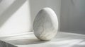Large, white marble egg sits on a marble surface, bathed in bright, dramatic light filtering through a nearby window, creating an Royalty Free Stock Photo