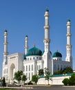 A large white mosque with beautiful green domes and four tall minarets under a blue sky.