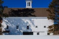 Large white New England barn in a snowy field aganst a deep blue late winters sky