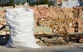 A large white plastic sack full of rubble stands in front of a demolished house with red bricks in the background