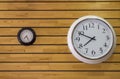 Large white round clock close up and a black small clock with arrows on the yellow wall of wooden planks. horizontal lines. Royalty Free Stock Photo