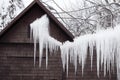 Large white snow ice icicles on wooden house on roof and wire.