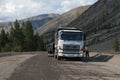 A white truck stands on the road and people prepare for road works in the mountains