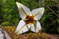 A large white and yellow metal flower sculpture in the garden surrounded by lush green trees and plants Royalty Free Stock Photo