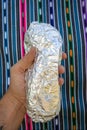 Hand Holding a Large Whole California-style Burrito Wrapped in Foil