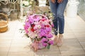 A large wicker basket full of colorful flowers near woman legs