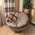 Large wicker round rattan chair with a warm plaid blanket in a room with a Christmas tree Royalty Free Stock Photo