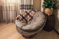 Large wicker round rattan chair with a warm plaid blanket in a room with a Christmas tree Royalty Free Stock Photo