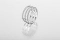 A large women`s ring with diamonds in white gold stands half a turn on a shiny metallic textured background.