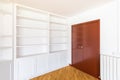 Large wooden closed mahogany door with a brass handle for opening. Along the wall is a white open cabinet with shelves