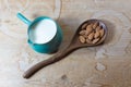 Large wooden spoon with almonds beside a ceramic bowl pitcher of almond milk on a rustic wood table background Royalty Free Stock Photo