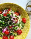 Large yellow bowl with salad, cabbage, tomatoes, capers, red onion, salad dressing in a glass, olive oil, healthy food