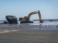 Large yellow excavator digs up sand at the edge of the ocean with a near by