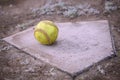 A large, yellow softball rests on home plate.