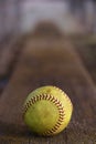 A yellow softball rests on the wooden bench in the dugout.