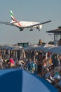 Boeing 777-31H(ER) of Emirates airlines landing over crowded Mackenzie Beach at Glafcos Clerides