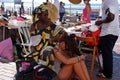 African woman making braids in the side walk next to the beach to a young female tourist