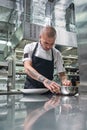 Last details. Vertical portrait of attractive male chef with beautiful tattoos on his arms garnishing his dish while Royalty Free Stock Photo