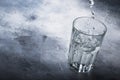 Last drops of pure water are poured into large glass cup on gray table background, selective focus Royalty Free Stock Photo