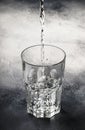 Last drops of pure water are poured into large glass cup on gray table background, selective focus Royalty Free Stock Photo