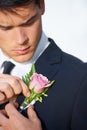 Last minute adjustments. A handsome young groom pinning a pink rose to his jacket.