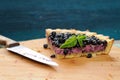 Last piece of blueberry pie decorated with basil leaves and knife on wooden board
