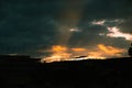 The last rays of the sunset illuminate the clouds in orange and show the silhouette of the roof of the building. Photo