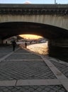 The last sunset light on the Seine as tourists walk under a bridge on the Left Bank