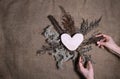 Lasting faded sustainable flowers with wooden heart on natural canvas background. Human hands making composition of dried flowers