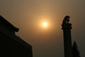 The late afternoon sun pierces through the Beijing haze, creating a golden light over the dragon pillar