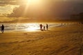 A family father, mother and child on the beach sand under the strong light of the sunset. Vibrant orange sky.