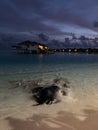 Late evening in the Maldives. Overwater villas with lights on, azure Indian Ocean waters with stingrays and little sharks swimming