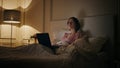Late freelancer working home resting in bed. Serious woman typing laptop message Royalty Free Stock Photo