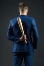 Latent aggression. Businessman or man in formal suit hides wooden bat behind back, dark background. Hidden danger