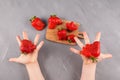 Latest trend - Eating ugly fruits and vegetables. Children`s hands offer ripe funny strawberries of unusual shape. Gray backgroun