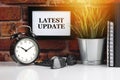 LATEST UPDATE text with alarm clock, books and vase on brick background Royalty Free Stock Photo