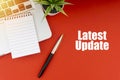 LATEST UPDATE text with notepad, laptop, fountain pen and decorative plant on red background Royalty Free Stock Photo