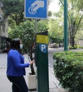 Latin adult woman with protection mask paying public parking on the street, new normal covid-19 Royalty Free Stock Photo