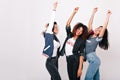 Latin, african and asian girls standing in the same pose with smile and hands up. Indoor portrait of international