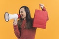 Latin-American cheerful girl holding a paper package bag after shopping and announcing sale in a megaphone, studio