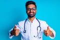 latin american student male in white coat and eyes glasses showing thumbs up in studio blue background Royalty Free Stock Photo