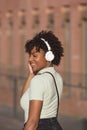 Latin American teenage girl with curly hair listening to music on smartphone wears headphones on the street Royalty Free Stock Photo