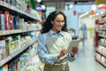 Latin American woman seller happy and smiling uses tablet computer in supermarket to check stock availability, shop Royalty Free Stock Photo