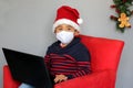 Latin boy with protection mask and santa claus hat in video call with laptop, new normal covid-19 and christmas decoration Royalty Free Stock Photo