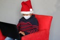 Latin boy with protection mask and santa claus hat in video call with laptop, new normal covid-19 and christmas decoration Royalty Free Stock Photo