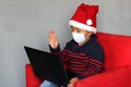 Latin boy with protection mask and santa claus hat in video call with laptop, new normal covid-19 and christmas decoration Royalty Free Stock Photo